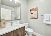 Thumbnail 12 of 37 - A bathroom with a toilet, sink, mirror, and towel rack at The Ashton at East Park Apartments, Kennesaw