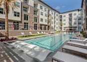 Thumbnail 22 of 47 - Swimming pool with lounge chairs in front of an apartment building at The Monroe Apartments, Texas, 78741