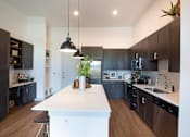 Thumbnail 7 of 47 - a large kitchen with a white island and dark cabinets at The Monroe Apartments, Austin, 78741