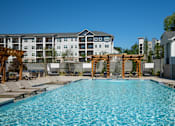 Thumbnail 31 of 37 - A large swimming pool with lounge chairs and a wooden pergola at The Ashton at East Park Apartments, Kennesaw, 30144