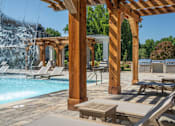 Thumbnail 34 of 37 - A poolside area with a waterfall and lounge chairs at The Ashton at East Park Apartments, Georgia