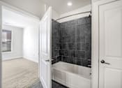 Thumbnail 21 of 64 - A bathroom with a black tiled shower area and a white bathtub.