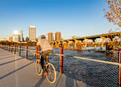 Thumbnail 31 of 37 - a man riding a bike on a bridge with a city in the background