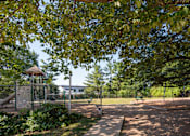 Thumbnail 7 of 14 - A playground with a swing set and a tree in the foreground.