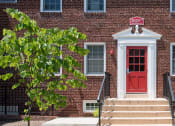 Thumbnail 2 of 12 - Clarendon Court Apartments a two-story red brick building with a red door and windows