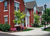 Thumbnail 4 of 5 - A row of red brick houses with green trees and bushes in front.