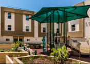 Thumbnail 4 of 10 - a large building with a playground and a green umbrella in the courtyard of Santa Cecilia Apartments