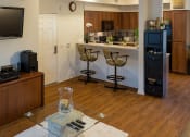 Thumbnail 2 of 6 - a living room with a television and a kitchen with wooden cabinets and a bar with stools