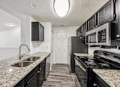 Thumbnail 10 of 31 - A kitchen with black cabinets and granite countertops at The Parkway at Hunters Creek, Orlando, 32837