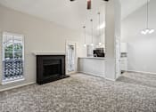 Thumbnail 18 of 27 - A living room with a fireplace and a kitchen area in the background.