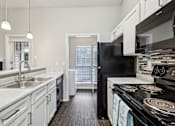 Thumbnail 21 of 27 - A black refrigerator sits in a kitchen with white cabinets and a black stove.
