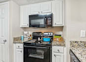 Thumbnail 8 of 51 - a kitchen with white cabinets and a black stove and microwave at The Glen at Highpoint, Dallas, 75243
