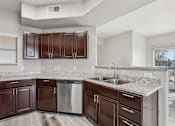 Thumbnail 28 of 105 - A kitchen with brown cabinets and a stainless steel dishwasher at Sweetwater At Metro North Apartments, Phoenix  85029