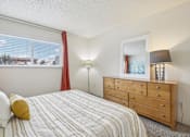 Thumbnail 10 of 45 - A bedroom with a bed, dresser, and window with red curtains at Spyglass Creek, Denver, 80224