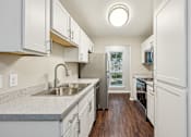 Thumbnail 24 of 27 - A kitchen with white cabinets and a wooden floor.