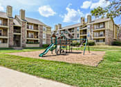 Thumbnail 39 of 39 - A playground with a green slide and a brown sandbox in front of apartment buildings.