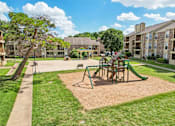 Thumbnail 36 of 39 - A playground with a green slide and a brown sandbox in the middle of a grassy area.