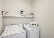 Thumbnail 16 of 105 - A laundry room with a washer and dryer and a laundry basket on top of the dryer at Sweetwater At Metro North Apartments, Phoenix, Arizona