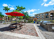 Thumbnail 45 of 50 - a picnic area with picnic tables and an umbrella in front of an apartment building at Pembroke Pines Landings, Pembroke Pines, FL, 33025