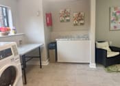 Thumbnail 48 of 51 - A laundry room with a washer and dryer, a bench, a couch, and a painting on the wall.