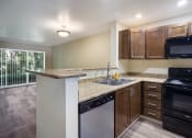 Thumbnail 4 of 31 - A kitchen with brown cabinets, black stove and stainless dishwasher at Arcadia Townhomes, Federal Way, WA