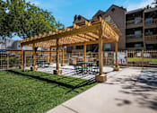 Thumbnail 21 of 23 - Outdoor wooden pergola with a table and chairs under and BBQ grills at Mountain Run Apartments, Albuquerque