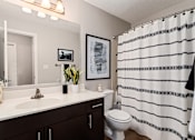 Thumbnail 15 of 43 - Bathroom with a white sink and toilet and a black and white shower curtain at University Ridge Apartments, Durham, NC, 27707