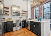 Thumbnail 1 of 42 - a kitchen with black and white cabinets and a large window at Riverwalk Apartments, Lawrence, MA