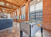Thumbnail 24 of 42 - a foosball table in a room with brick walls and a bar at Riverwalk Apartments, Lawrence, MA