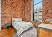Thumbnail 21 of 42 - a bedroom with a bed and a brick wall at Riverwalk Apartments, Lawrence, MA