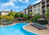 Thumbnail 46 of 46 - A swimming pool surrounded by lounge chairs and umbrellas in front of apartment buildings.