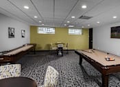 Thumbnail 26 of 27 - a game room with a shuffle board, seating, and games