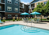 Thumbnail 11 of 22 - A swimming pool surrounded by chairs and umbrellas in front of a building.