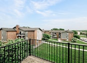 Thumbnail 11 of 24 - A balcony overlooks a grassy area with apartment buildings in the distance.