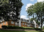 Thumbnail 13 of 24 - A large building with a red brick exterior and a balcony is surrounded by trees.