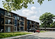 Thumbnail 8 of 24 - A black car is parked in front of a blue apartment building.