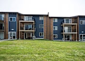 Thumbnail 22 of 24 - Apartment complex with blue and brown buildings and green grass in front.
