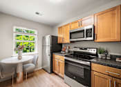 Thumbnail 40 of 64 - Bright kitchen at New Kent Apartments with stainless steel appliances, wood cabinetry, and cozy dining nook by a large window with natural light