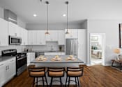 Thumbnail 1 of 34 - An L-shaped kitchen with a breakfast bar, two pendant lights, stainless steel appliances, hardwood-style flooring, and white cabinets.
