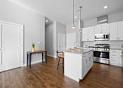 Thumbnail 5 of 34 - A modern kitchen with a breakfast bar, pendant lights, quartz countertops, stainless steel appliances, subway tile, and white cabinets near the entryway.