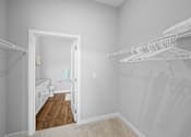 Thumbnail 8 of 34 - A spacious walk-in closet with clothing shelves near a doorway that leads to a private bathroom.