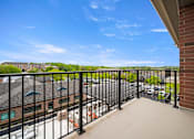 Thumbnail 10 of 39 - A balcony with a black railing overlooks a parking lot and buildings.