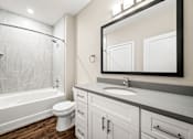 Thumbnail 29 of 34 - A white toilet sits in a bathroom next to a white bathtub.