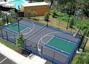Thumbnail 17 of 34 - An outdoor basketball court near a gated pool and a river with trees.