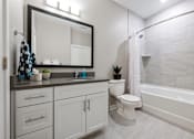 Thumbnail 9 of 39 - A bathroom with a white toilet, a sink, a mirror, and a bathtub.