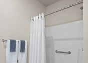Thumbnail 9 of 17 - a bathroom with a shower with a white shower curtain and towels