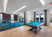 Thumbnail 11 of 34 - A clubhouse with a billiards table, a ping pong table, and a shuffleboard near doors leading to an outdoor community lounge.