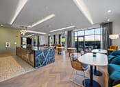 Thumbnail 18 of 34 - A community kitchen and resident lounge with a long bar, tables, chairs, and large windows.