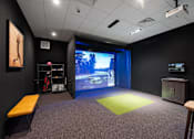 Thumbnail 12 of 34 - A multi-sport simulator projector screen in a community room with sports equipment.