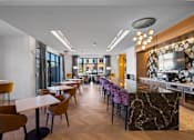 Thumbnail 16 of 34 - A long bar with modern purple barstools, tables and chairs, and a TV in a resident lounge with a community kitchen.